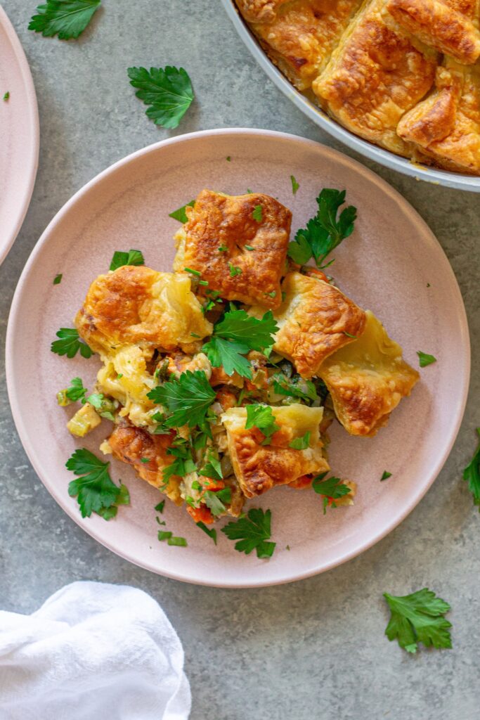 Overhead shot of vegan tofu pot pie with creamy veggie filling, topped with golden and flaky puff pastry squares, then garnished with fresh parsley.
