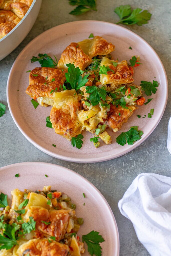 Overhead shot of vegan tofu pot pie with creamy veggie filling, topped with golden and flaky puff pastry squares, then garnished with fresh parsley.