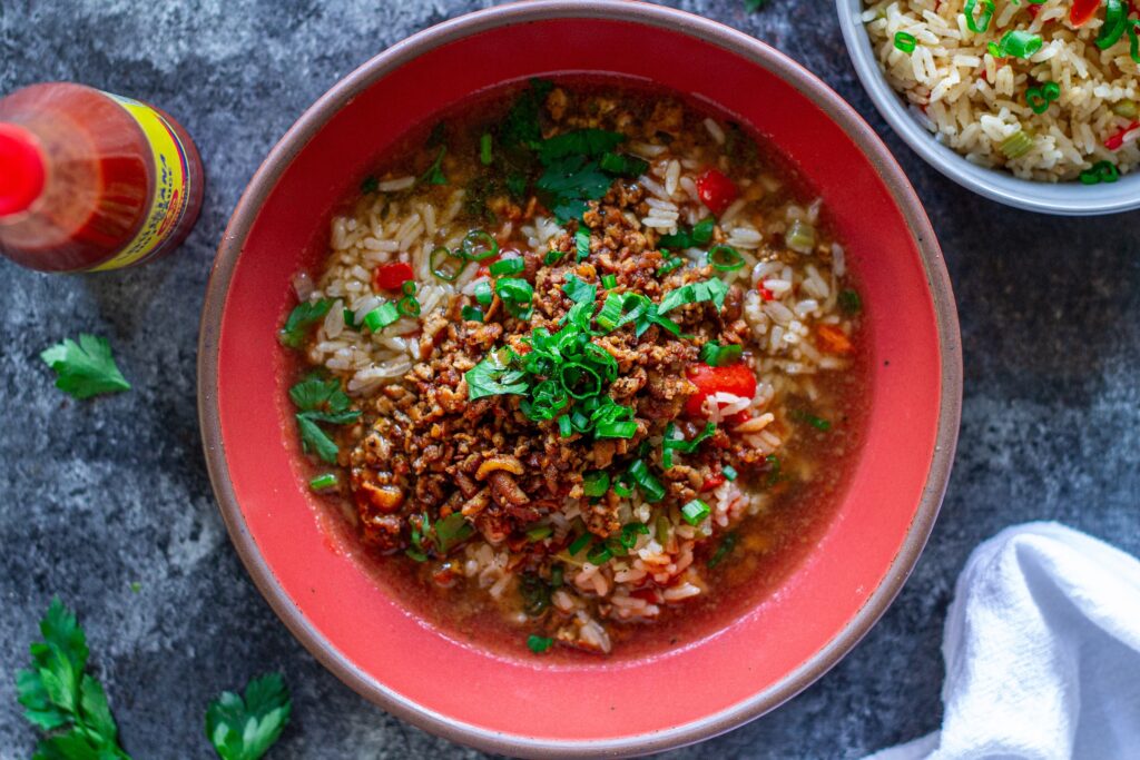 Bowl of crispy, blackened tofu and Cajun brothy rice topped with fresh green onion and parsley.