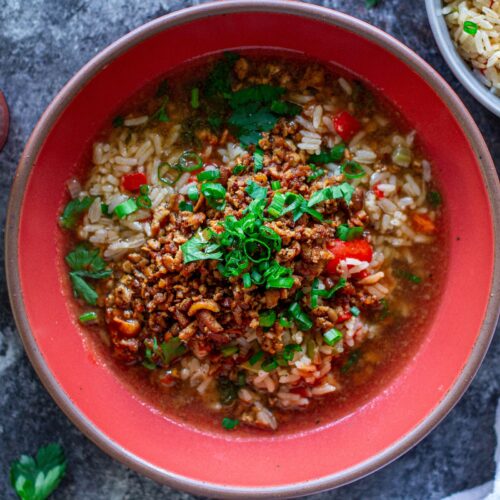 Bowl of crispy, blackened tofu and Cajun brothy rice topped with fresh green onion and parsley.