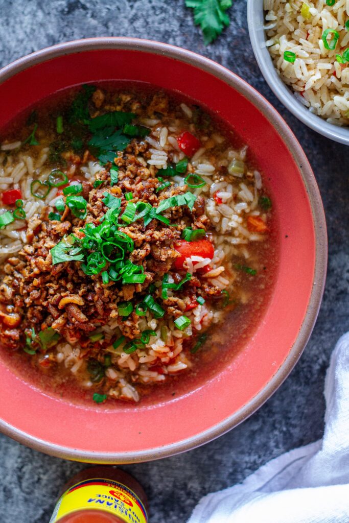 Bowl of crispy, blackened tofu and Cajun brothy rice topped with fresh green onion and parsley.