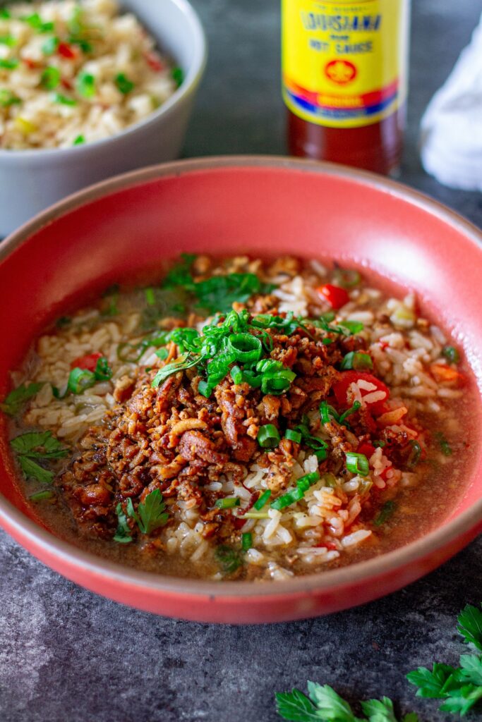 Bowl of crispy, blackened tofu and Cajun brothy rice topped with fresh green onion and parsley.