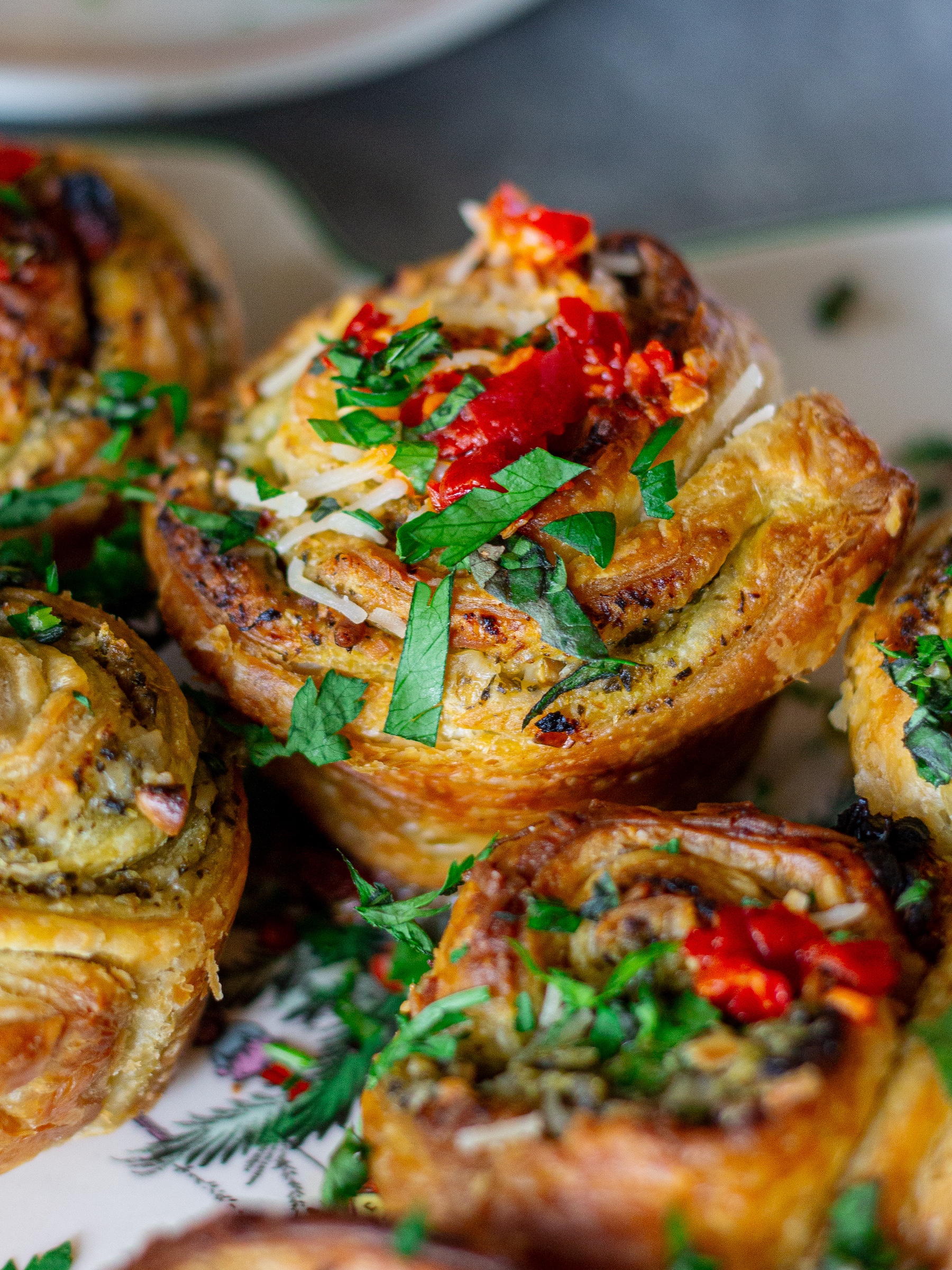 Close-up of flaky puff pastry pinwheel showing pesto and sun-dried tomato swirls with melted vegan parmesan.