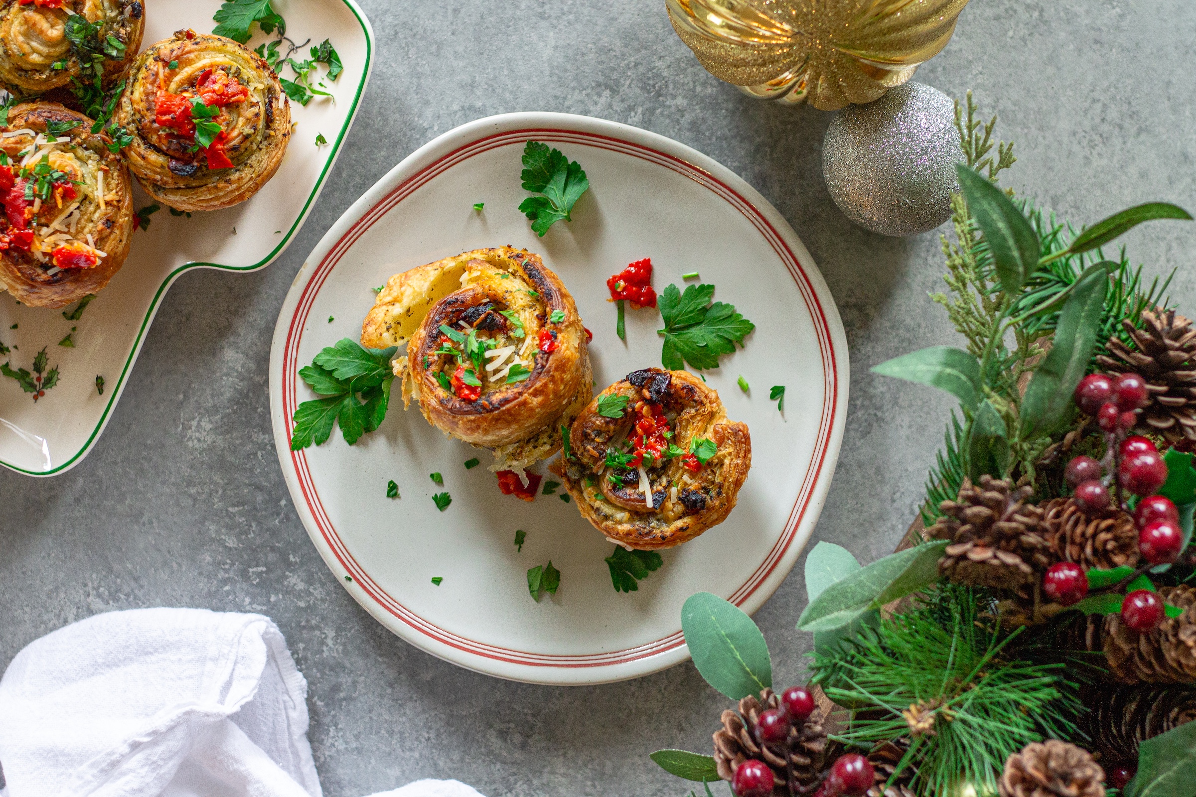 Golden vegan puff pastry pinwheels filled with pesto and sun-dried tomatoes on a parchment-lined baking sheet.