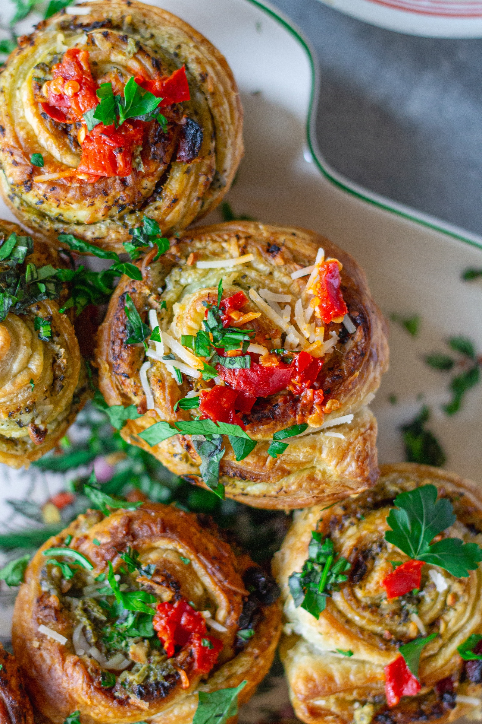 Close-up of flaky puff pastry pinwheel showing pesto and sun-dried tomato swirls with melted vegan parmesan.
