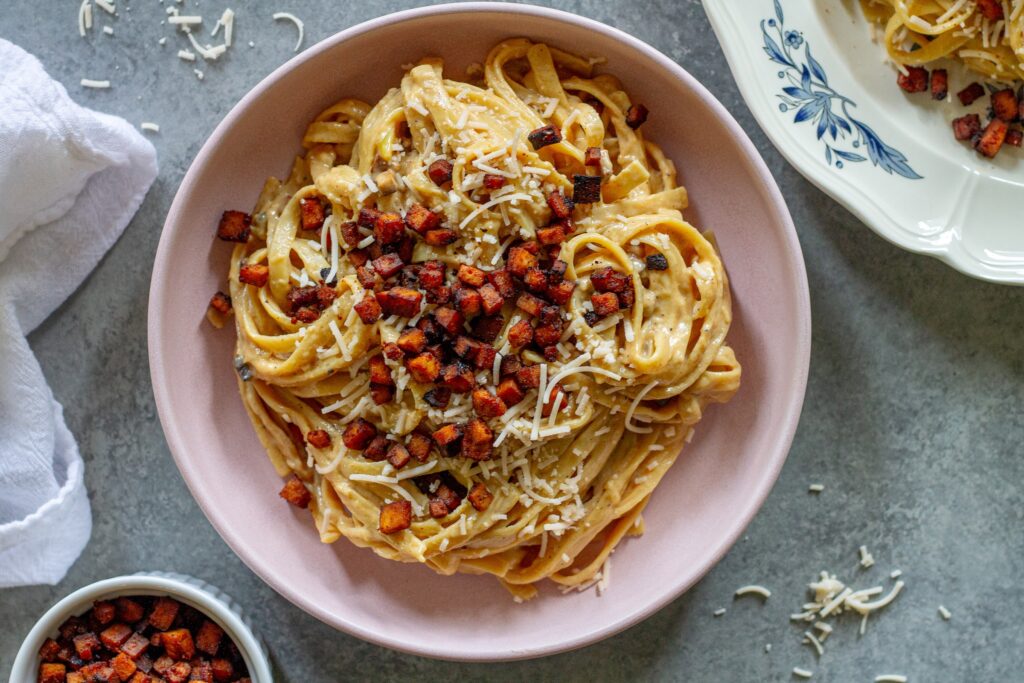 Vegan carbonara‑inspired fettuccine topped with crispy tofu bacon and a sprinkle of vegan Parmesan.