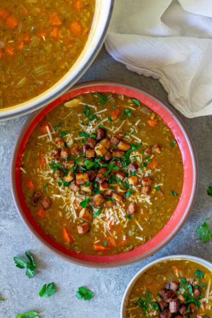 Bowl of creamy vegan split‑pea soup garnished with crispy tofu “bacon” and fresh parsley.