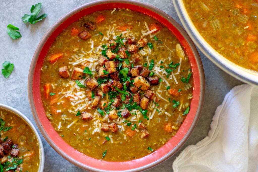 Bowl of creamy vegan split‑pea soup garnished with crispy tofu “bacon” and fresh parsley.