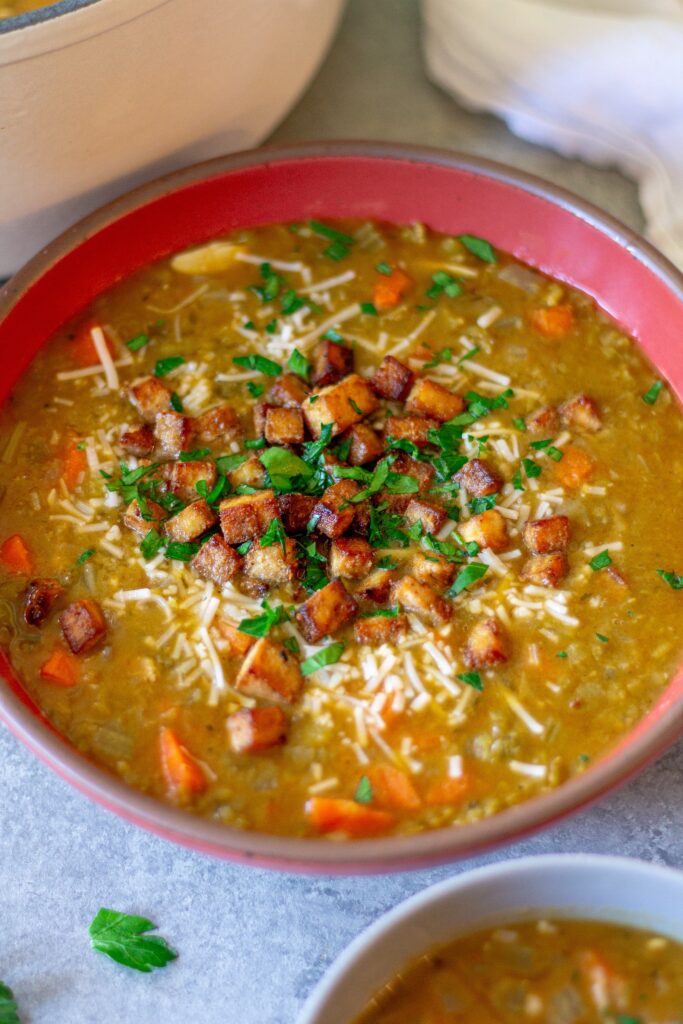 Bowl of creamy vegan split‑pea soup garnished with crispy tofu “bacon” and fresh parsley.