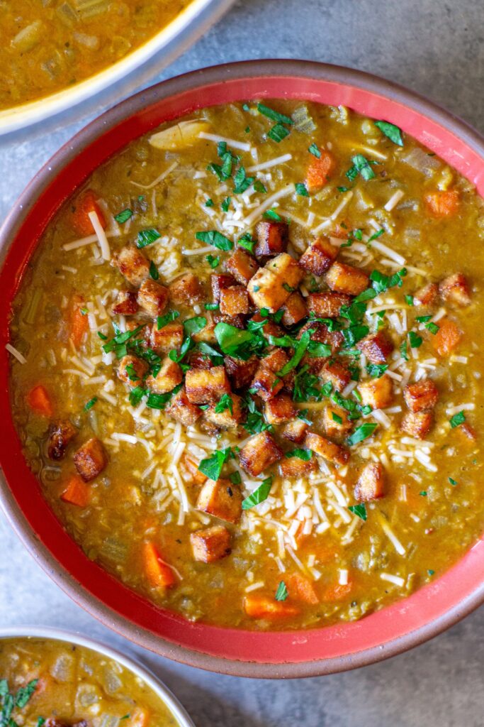 Bowl of creamy vegan split‑pea soup garnished with crispy tofu “bacon” and fresh parsley.