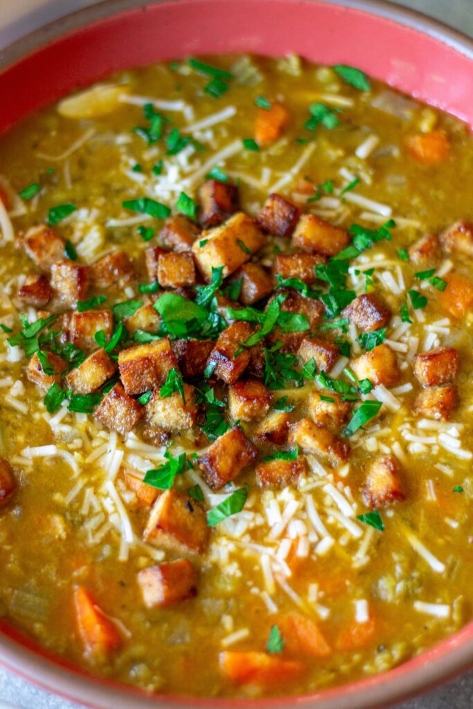 Bowl of creamy vegan split‑pea soup garnished with crispy tofu “bacon” and fresh parsley.