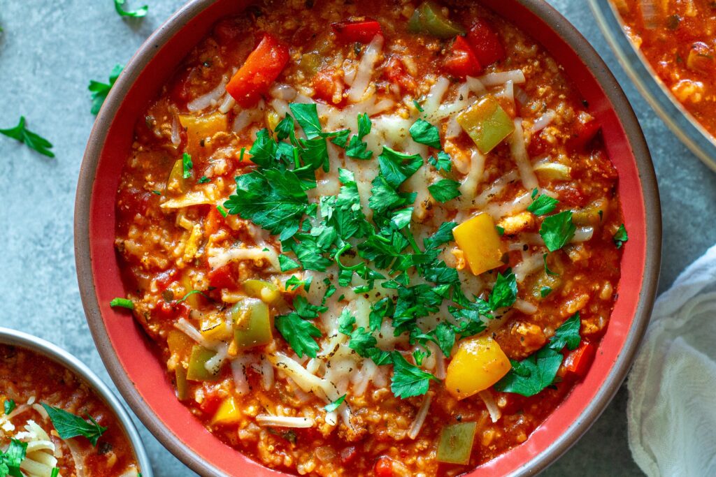 Steaming bowl of vegan stuffed pepper soup topped with fresh parsley and vegan mozzarella shreds.