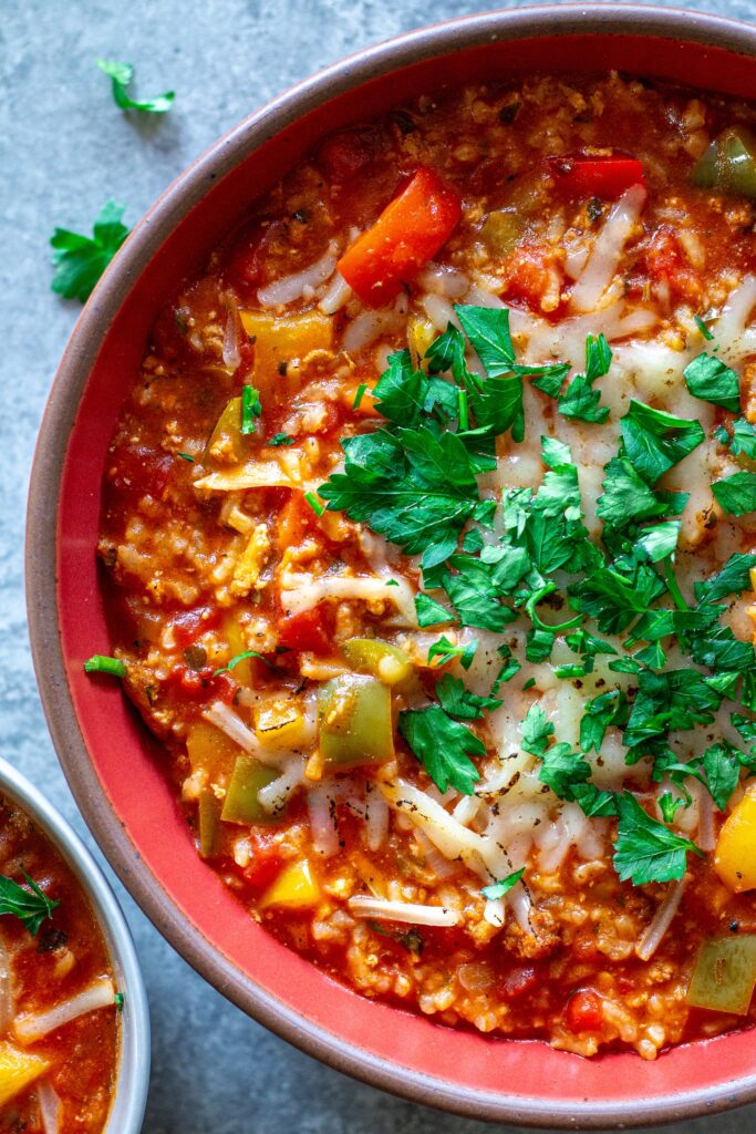 Steaming bowl of vegan stuffed pepper soup topped with fresh parsley and vegan mozzarella shreds.