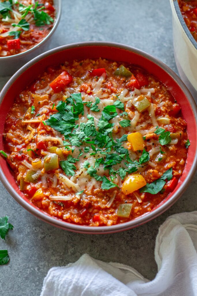 Steaming bowl of vegan stuffed pepper soup topped with fresh parsley and vegan mozzarella shreds.
