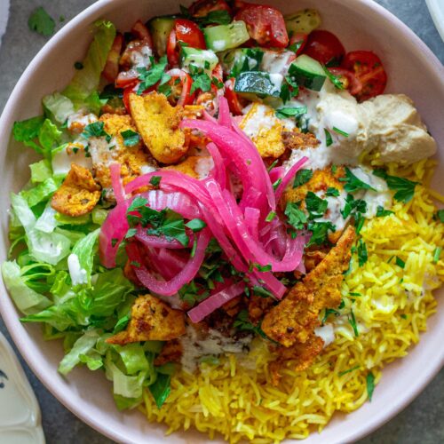 Vibrant tofu shawarma bowl featuring turmeric rice, spiced tofu, cucumber tomato salad, lettuce, and creamy garlic sauce