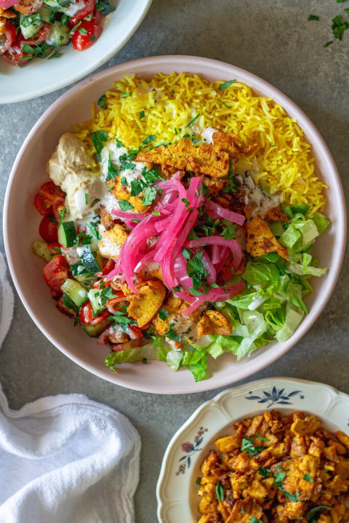 Vibrant tofu shawarma bowl featuring turmeric rice, spiced tofu, cucumber tomato salad, lettuce, and creamy garlic sauce.
