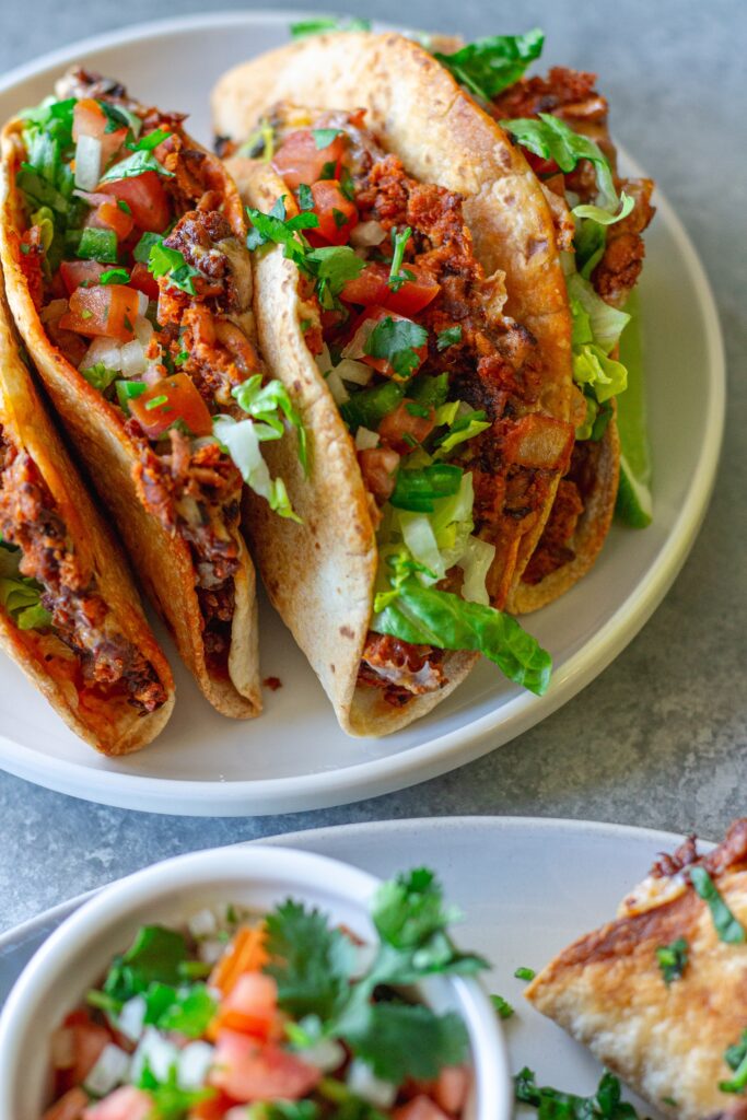 crispy baked chipotle tofu tacos garnished with cilantro and served with a side of avocado cream sauce and pico de Gallo.