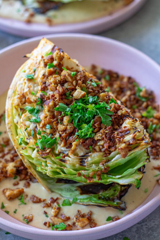 Grilled cabbage wedges topped with maple Dijon tofu and creamy white bean garlic sauce on a plate.