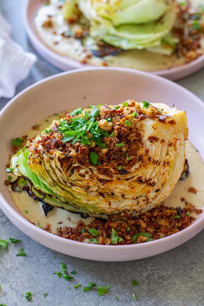 Grilled cabbage wedges topped with maple Dijon tofu and creamy white bean garlic sauce on a plate.