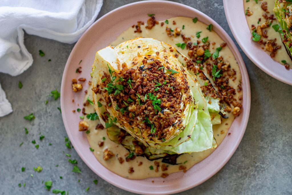 Grilled cabbage wedges topped with maple Dijon tofu and creamy white bean garlic sauce on a plate.