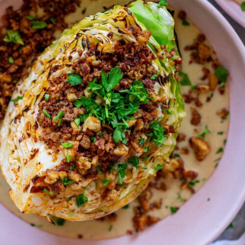 Grilled cabbage wedges topped with maple Dijon tofu and creamy white bean garlic sauce on a plate.
