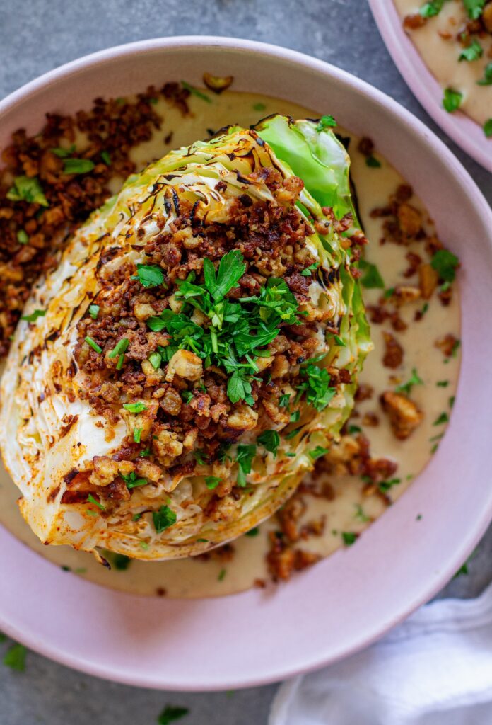 Grilled cabbage wedges topped with maple Dijon tofu and creamy white bean garlic sauce on a plate.