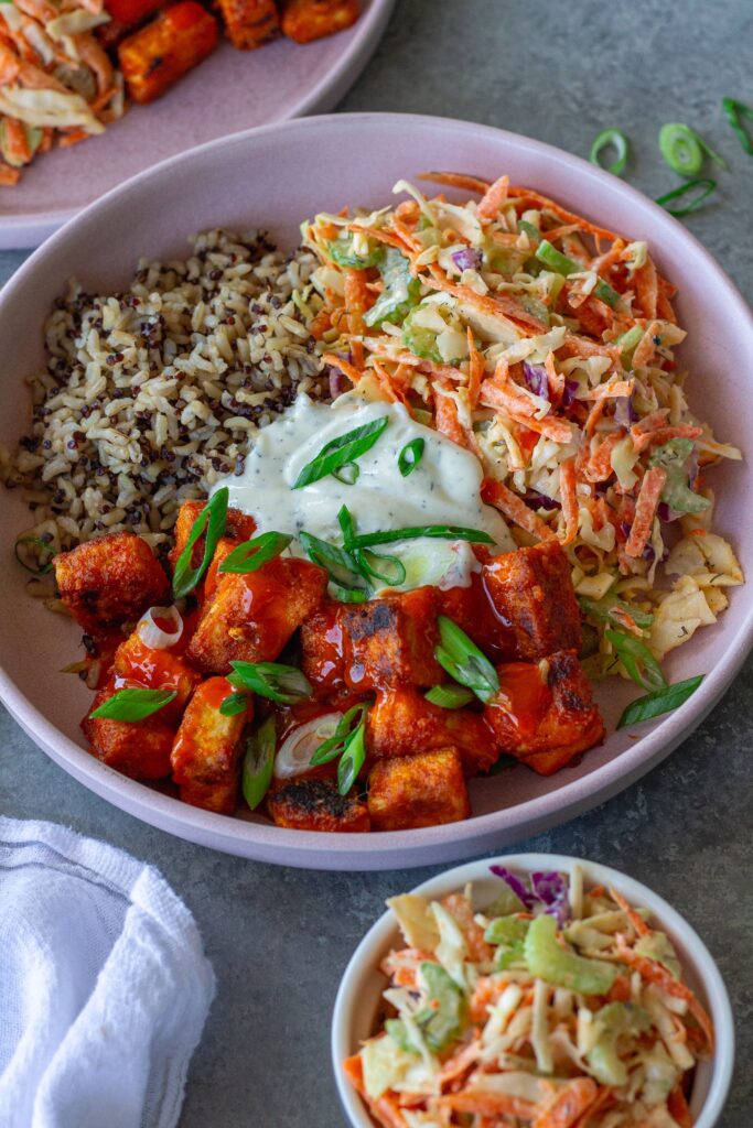 Close-up of a colorful Buffalo Tofu Ranch Bowl with crispy golden tofu, creamy ranch slaw, and quinoa/brown rice mixture, garnished with green onions.