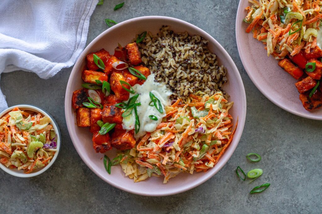 Close-up of a colorful Buffalo Tofu Ranch Bowl with crispy golden tofu, creamy ranch slaw, and quinoa/brown rice mixture, garnished with green onions.