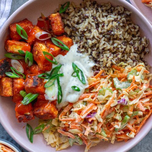 Close-up of a colorful Buffalo Tofu Ranch Bowl with crispy golden tofu, creamy ranch slaw, and quinoa/brown rice mixture, garnished with green onions.