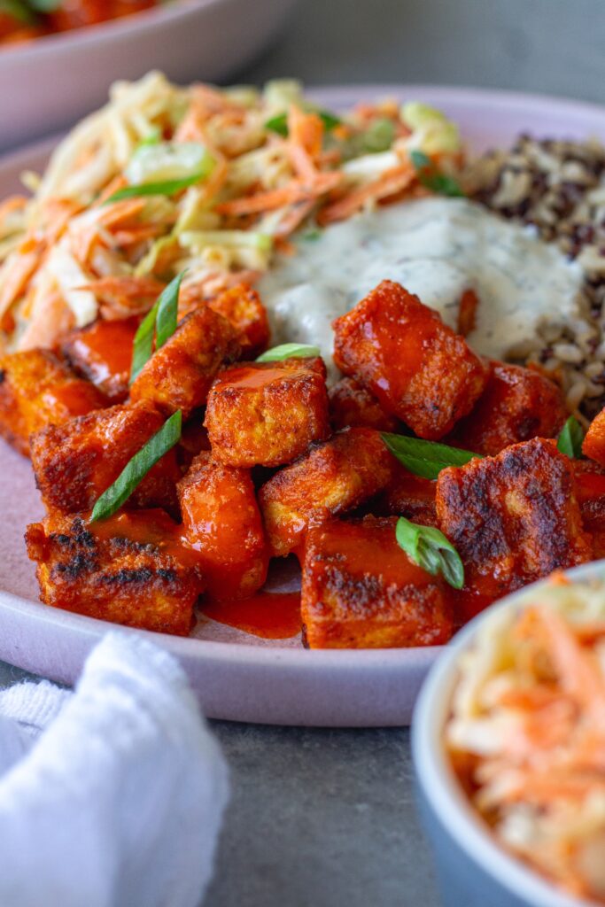 Close-up of a colorful Buffalo Tofu Ranch Bowl with crispy golden tofu, creamy ranch slaw, and quinoa/brown rice mixture, garnished with green onions.