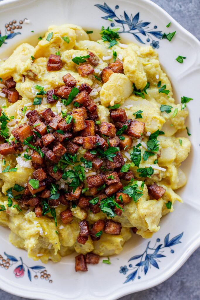 Close-up of creamy vegan carbonara butter beans topped with crispy golden tofu bacon bits, grated vegan parmesan, and fresh parsley.