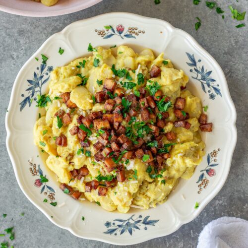 Close-up of creamy vegan carbonara butter beans topped with crispy golden tofu bacon bits, grated vegan parmesan, and fresh parsley.