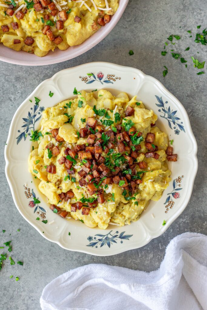 Close-up of creamy vegan carbonara butter beans topped with crispy golden tofu bacon bits, grated vegan parmesan, and fresh parsley.