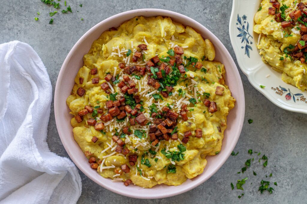 Close-up of creamy vegan carbonara butter beans topped with crispy golden tofu bacon bits, grated vegan parmesan, and fresh parsley.