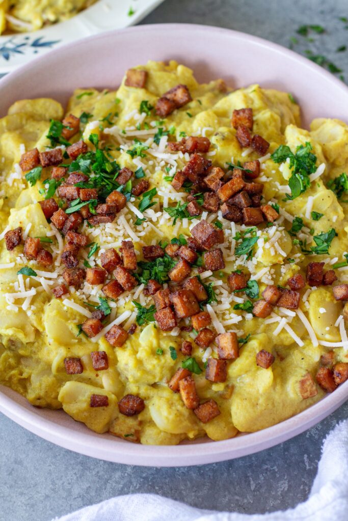 Close-up of creamy vegan carbonara butter beans topped with crispy golden tofu bacon bits, grated vegan parmesan, and fresh parsley.