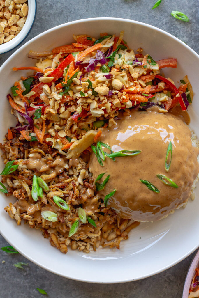 Bowl of crispy shredded tofu peanut bowls with creamy peanut sauce and colorful slaw, garnished with green onion and crushed peanuts.