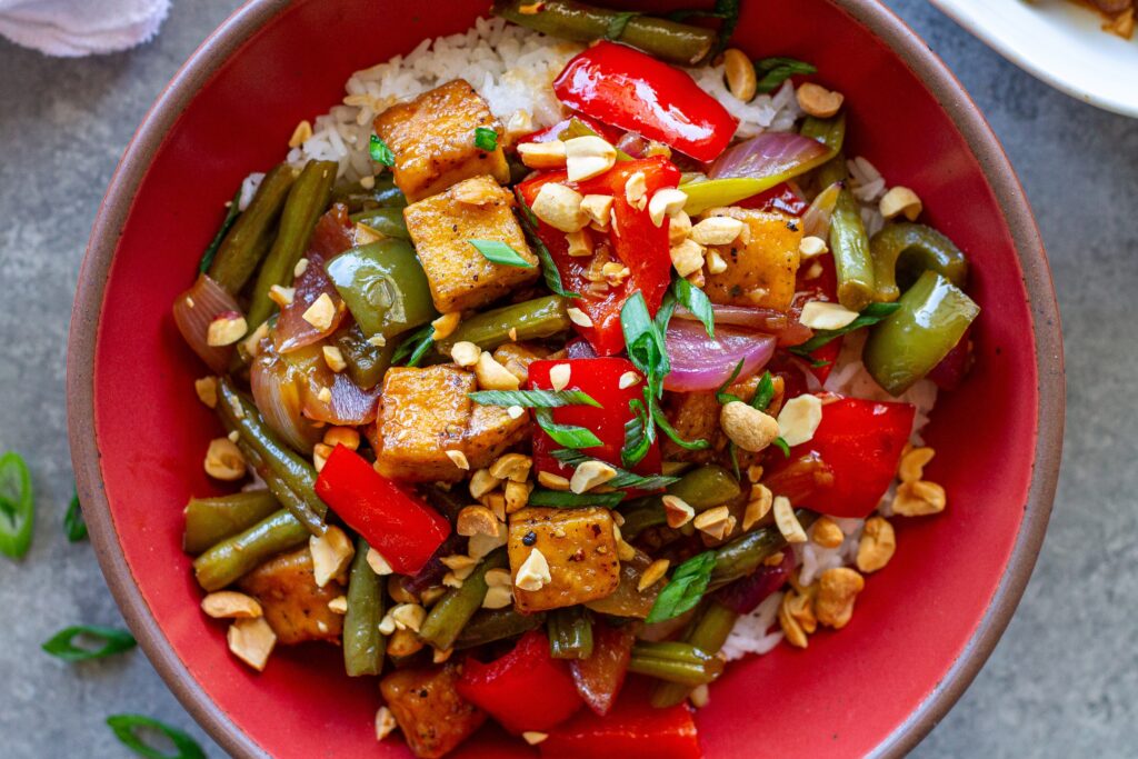 Golden crispy Kung Pao Tofu stir fry served over white rice with crushed peanuts and green onions.