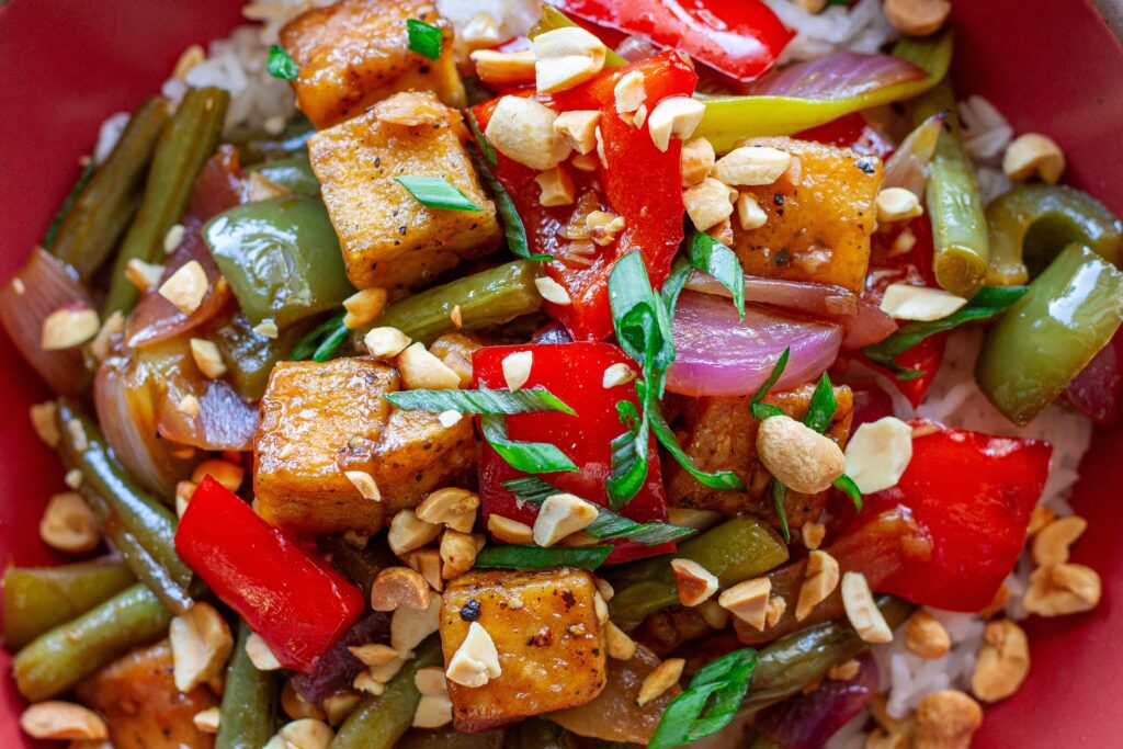 Golden crispy Kung Pao Tofu stir fry served over white rice with crushed peanuts and green onions.