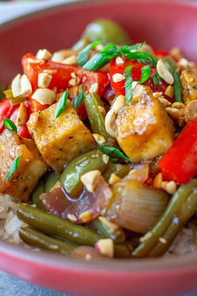 Golden crispy Kung Pao Tofu stir fry served over white rice with crushed peanuts and green onions.