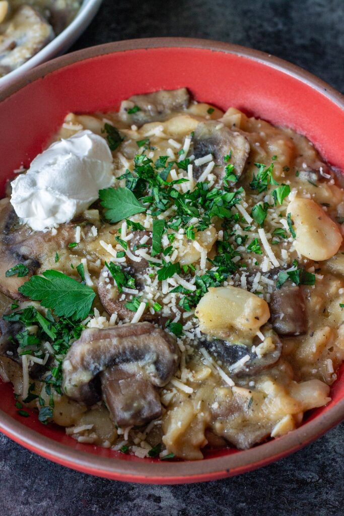 Creamy butter bean and mushroom stroganoff served in a bowl with fresh parsley, parmesan, and a dollop of sour cream.