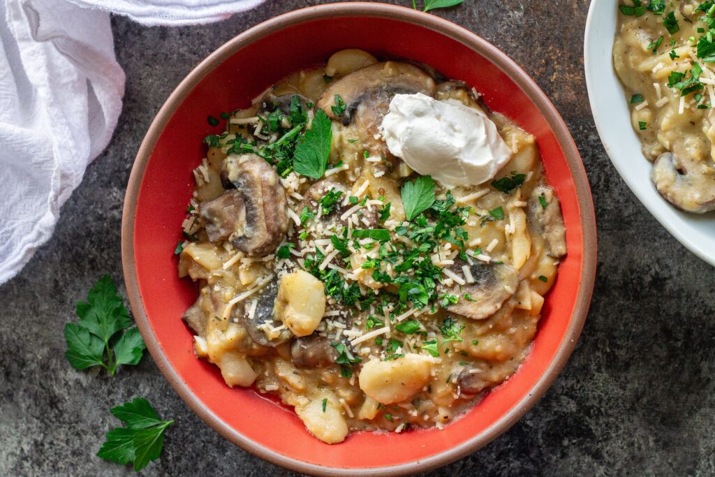 Creamy butter bean and mushroom stroganoff served in a bowl with fresh parsley, parmesan, and a dollop of sour cream.