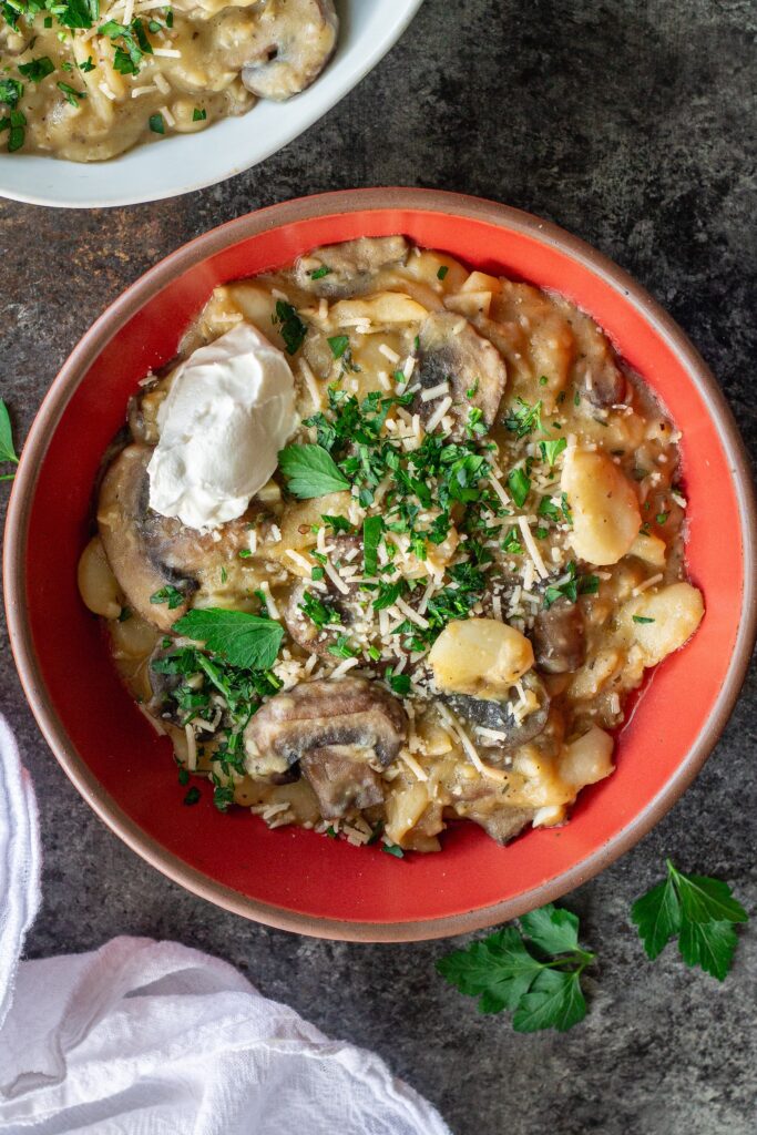Creamy butter bean and mushroom stroganoff served in a bowl with fresh parsley, parmesan, and a dollop of sour cream.