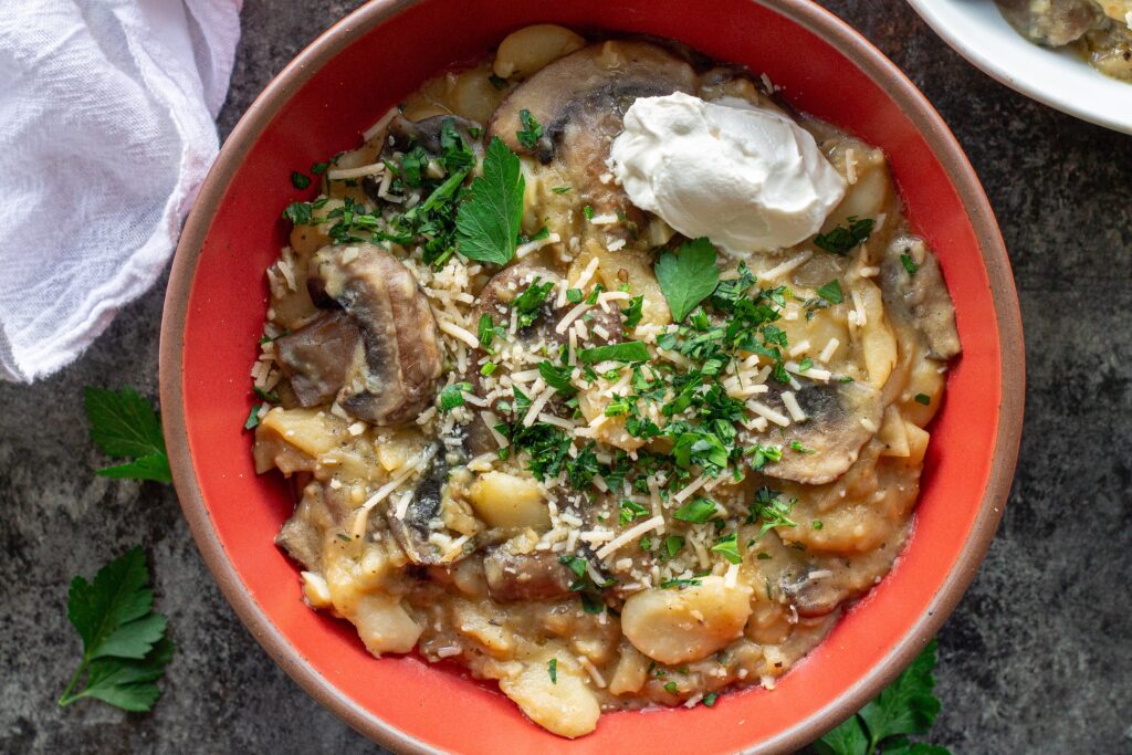 Creamy butter bean and mushroom stroganoff served in a bowl with fresh parsley, parmesan, and a dollop of sour cream.