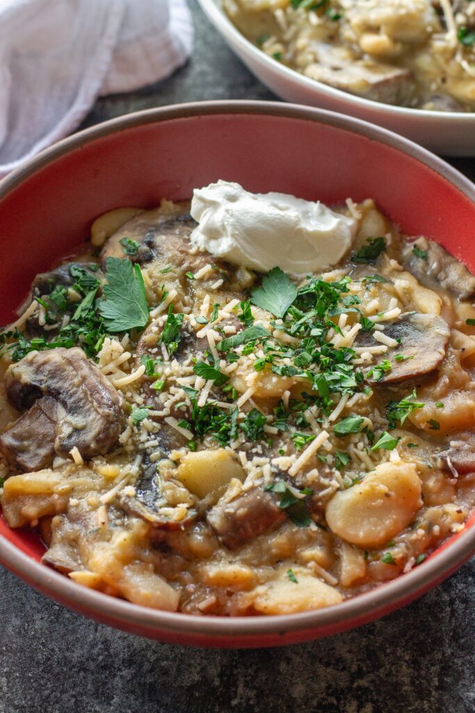 Creamy butter bean and mushroom stroganoff served in a bowl with fresh parsley, parmesan, and a dollop of sour cream.