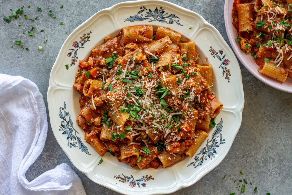 A serving of one-pot rigatoni bolognese topped with fresh parsley and vegan parmesan cheese.