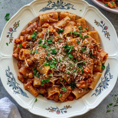 A serving of one-pot rigatoni bolognese topped with fresh parsley and vegan parmesan cheese.