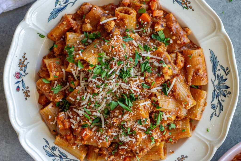 A serving of one-pot rigatoni bolognese topped with fresh parsley and vegan parmesan cheese.