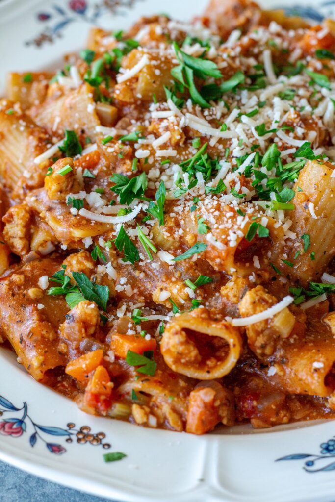 A serving of one-pot rigatoni bolognese topped with fresh parsley and vegan parmesan cheese.