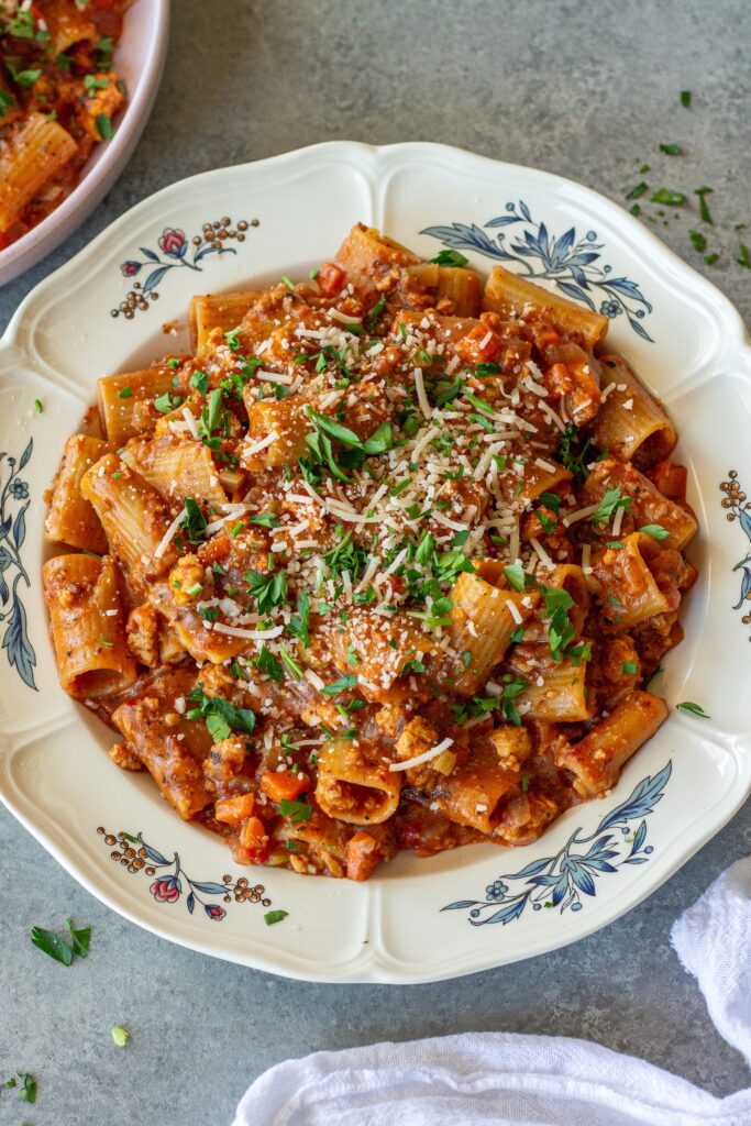 A serving of one-pot rigatoni bolognese topped with fresh parsley and vegan parmesan cheese.