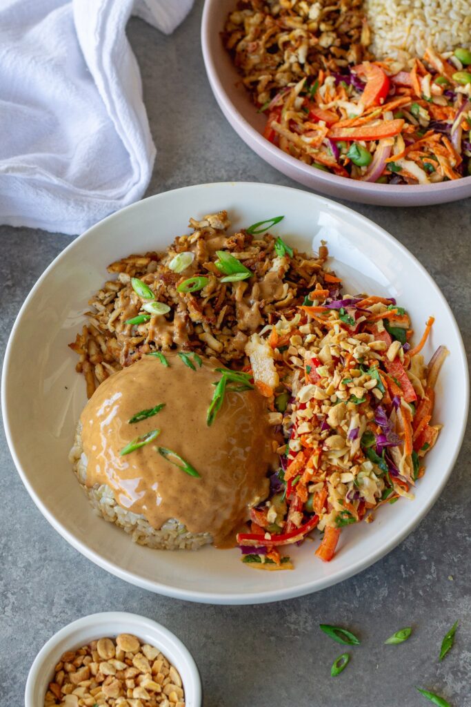 Bowl of crispy shredded tofu peanut bowls with creamy peanut sauce and colorful slaw, garnished with green onion and crushed peanuts.